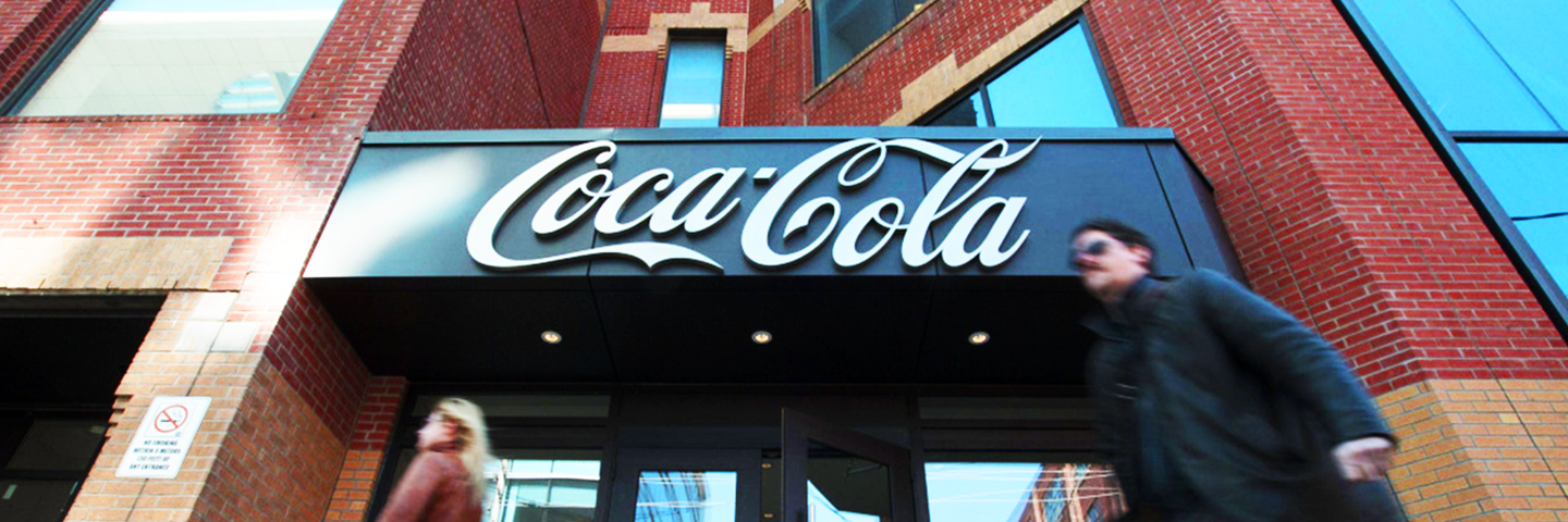 Les gens marchent devant un bâtiment en briques rouges avec un grand panneau Coca-Cola sur la façade