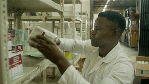 Un agent de santé africain empile des boîtes de médicaments sur une étagère, il porte une blouse blanche